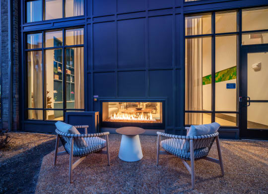 a fireplace in front of a blue building with chairs and a table at Preston Ridge, Cary, NC