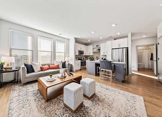 A modern living room with a grey sofa, a wooden coffee table, and a kitchen area in the background.