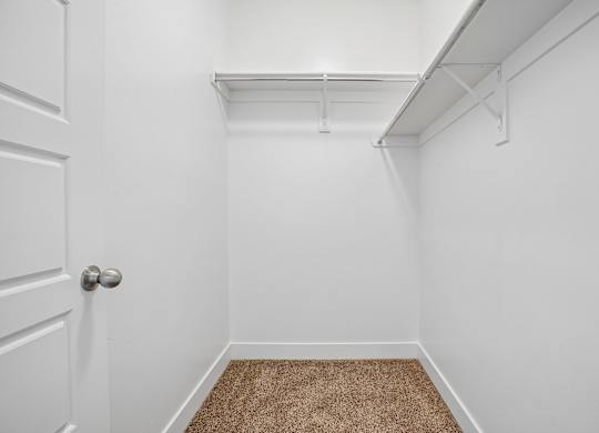 A white door is on the left of a room with a brown carpet.