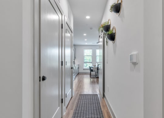 a long hallway with white walls and a door to a kitchen