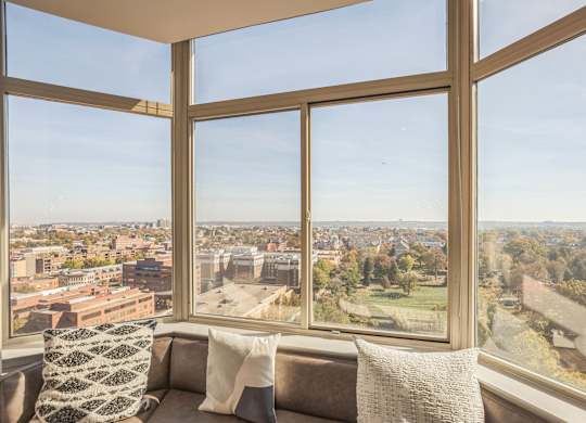 A couch with a pillow sits in front of a large window with a view of a city.