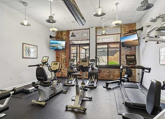A gym with a brick wall and a row of treadmills.