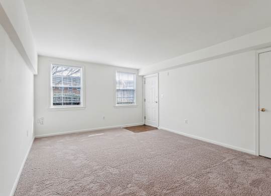 A room with a carpeted floor and two windows.