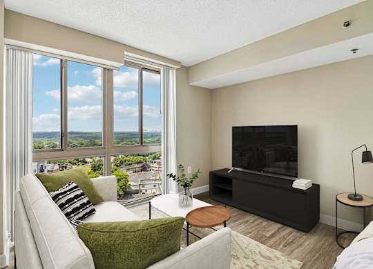 A living room with a couch, a chair, a coffee table, a television, and a window with a view of the city.