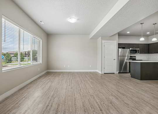 A spacious room with wooden flooring and a kitchen area in the background.