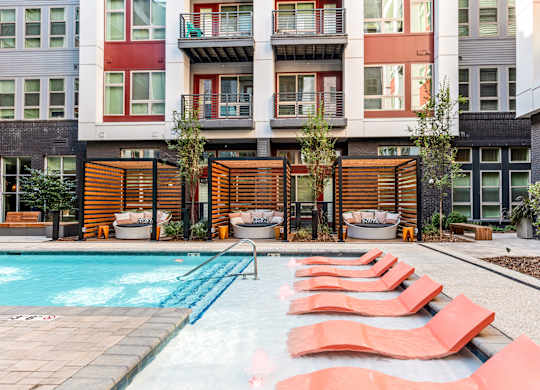 a pool with red lounge chairs in front of an apartment building