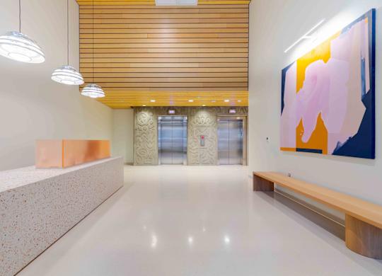 A hallway with a white floor, a bench, and a painting on the wall.