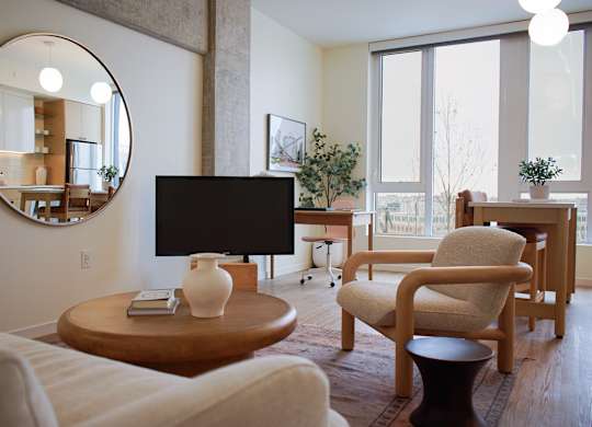 A living room with a white couch, a wooden chair, a round mirror, and a flat screen TV.