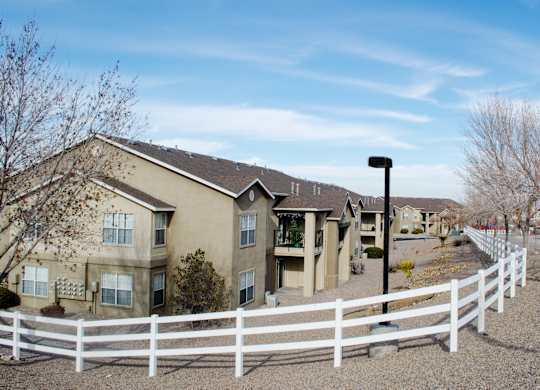 A white fence surrounds a building with a brown roof at Arrowhead Ridge Apartments, New Mexico 87124