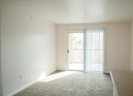 A room with a carpeted floor and a sliding glass door at Arrowhead Ridge Apartments, Rio Rancho, New Mexico