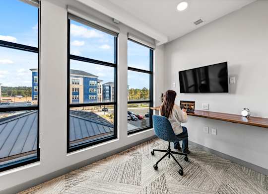 A woman is sitting at a desk in a private office with a large window at Preston Ridge Apartments Cary, NC.