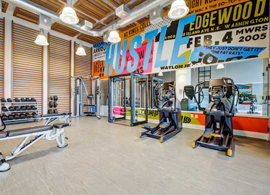a gym with cardio machines and weights on the floor and a wall with a mural at Coda at Bryant Street, Washington, 20002
