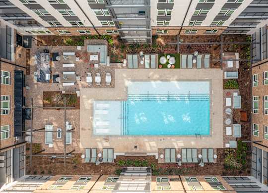 A large swimming pool is surrounded by a patio with lounge chairs and umbrellas at Hawkins Press Apartments, Charlotte, 28203