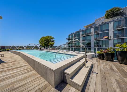 A wooden deck with a pool and a building in the background.