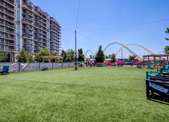 A grassy field with a bench and a bridge in the background.