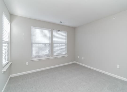 an empty bedroom with two windows and white carpeting at The Fields at Lorton Station, Lorton, VA