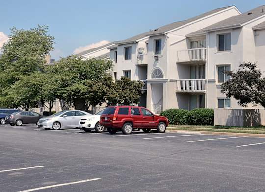 A red car is parked in a parking lot in front of apartment buildings.