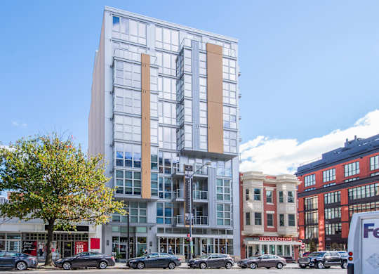 A modern glass building stands in front of a row of older buildings.