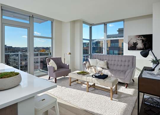 A modern living room with a grey sofa, a white table, and a large window with a view of the city.