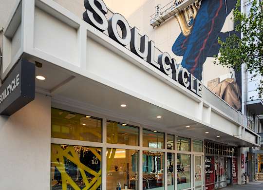 A storefront with a large yellow and black window and a sign that reads Soulcycle.