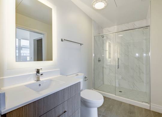 A bathroom with a toilet, sink, mirror, and shower.
