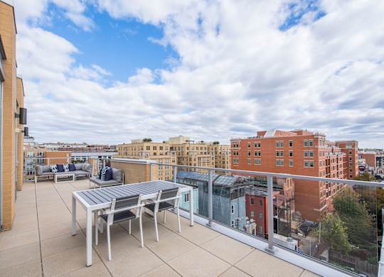 A balcony with a table and chairs overlooks a cityscape.