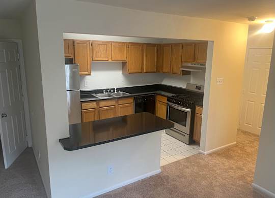A kitchen with wooden cabinets and black countertops at Shenandoah Station Apartments, Virginia