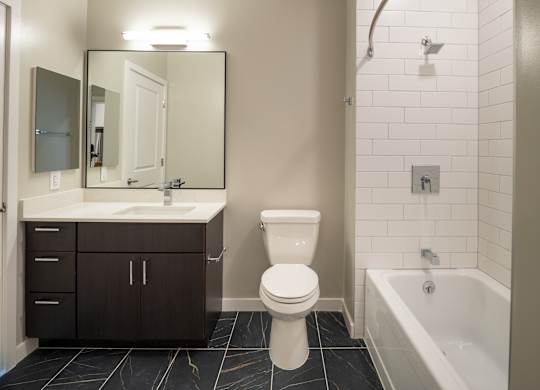 A white toilet sits in a bathroom next to a sink and a bathtub.