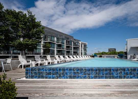 A swimming pool surrounded by white chairs and a modern building in the background. at Dock 79, District of Columbia