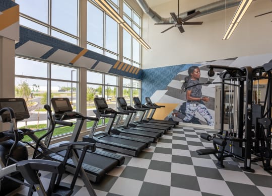 a woman runs on a treadmill in front of a wall of windows with a mural of a  at Woodmore Grand, Bowie, 20721