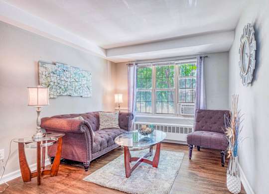 A living room with a purple couch, a glass table, and a clock on the wall at Huntwood Courts Apartments, Washington