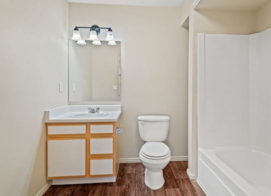 A white toilet sits next to a sink in a small bathroom. at Bluffs Apartments, Bluffdale, 84065