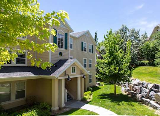 A house with a stone wall and a tree in front. at Bluffs Apartments, Utah, 84065