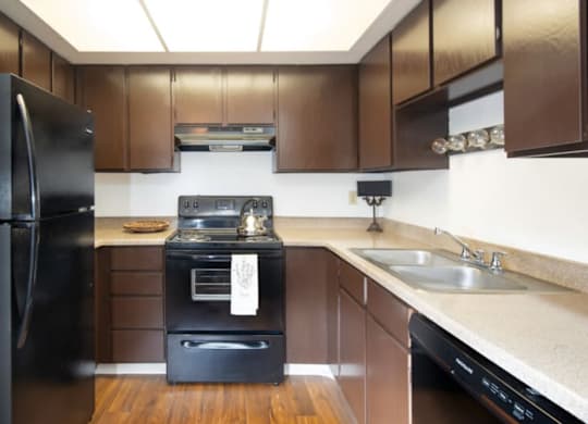 A black refrigerator is in a kitchen with brown cabinets.at Country Woods, Ogden, UT  
