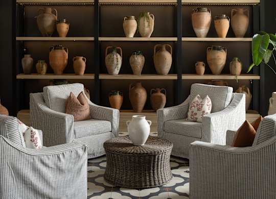 A room with a shelf full of vases and chairs.