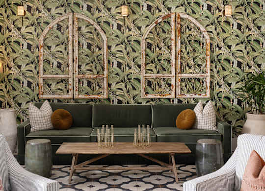 A living room with a green couch, a wooden coffee table, and a patterned wallpaper.
