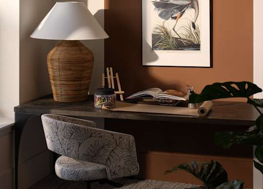A desk with a lamp, chair, and a painting of a bird.