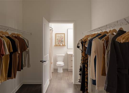 A hallway with clothes hanging on both sides and a toilet in the background.