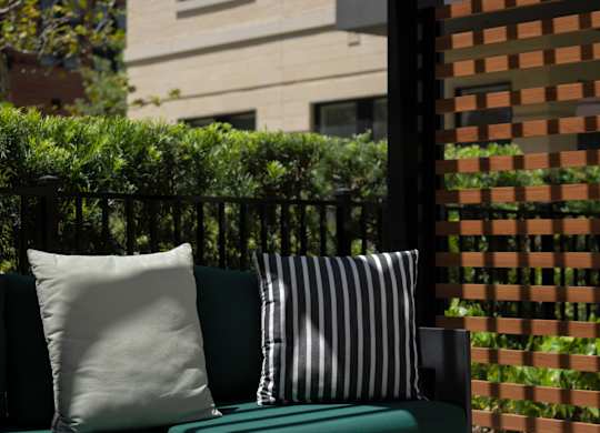 A white bench with a green cushion and a striped pillow sits on a patio.
