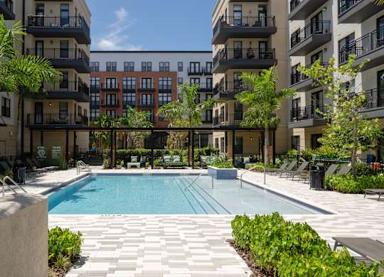 A swimming pool surrounded by apartment buildings and palm trees.