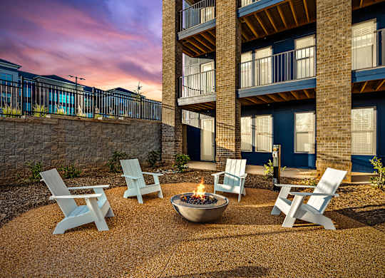 A fire pit sits in the middle of a gravel patio surrounded by four chairs.