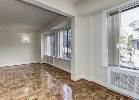 A room with a wooden floor and a window with a view of a house.