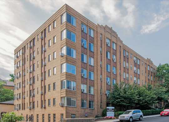 A tall brick building with many windows and cars parked in front.