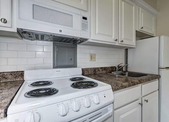 A white stove with four burners is in a kitchen with white cabinets.