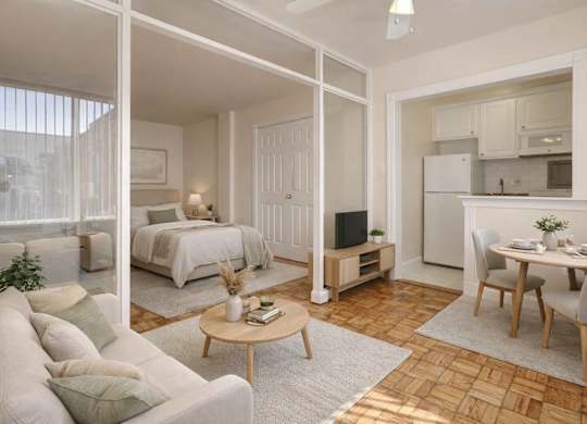 A well-lit, spacious living room with a couch, coffee table, and a bedroom area in the background.