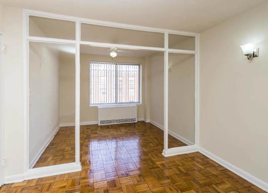 A room with white walls and wooden flooring with a window.