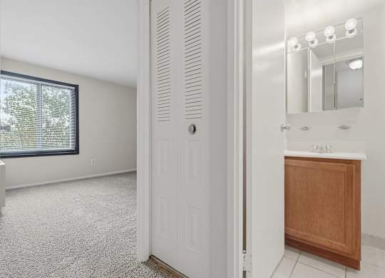 A white door is open to a bathroom with a sink and mirror.