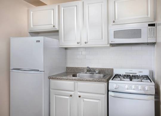 A white kitchen with a refrigerator, microwave, oven, and sink.