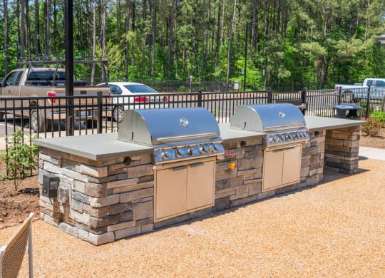 an outdoor kitchen with two grills next to a fence at Preston Ridge, Cary