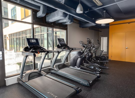 a gym with cardio equipment and a large window